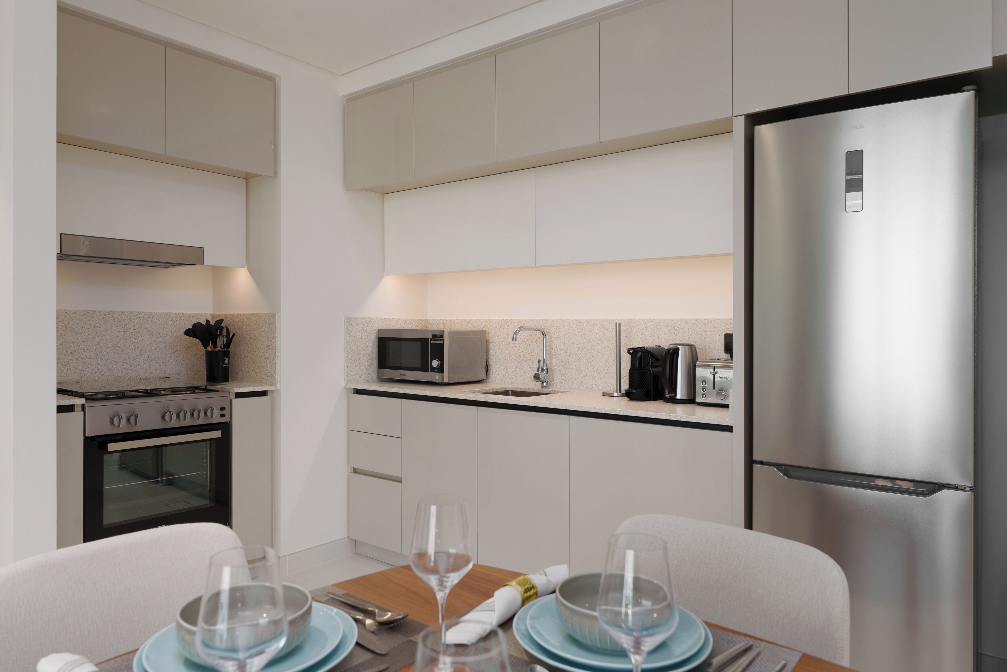 A modern kitchen with white cabinets, stainless steel appliances, and a dining area with a table set for two.