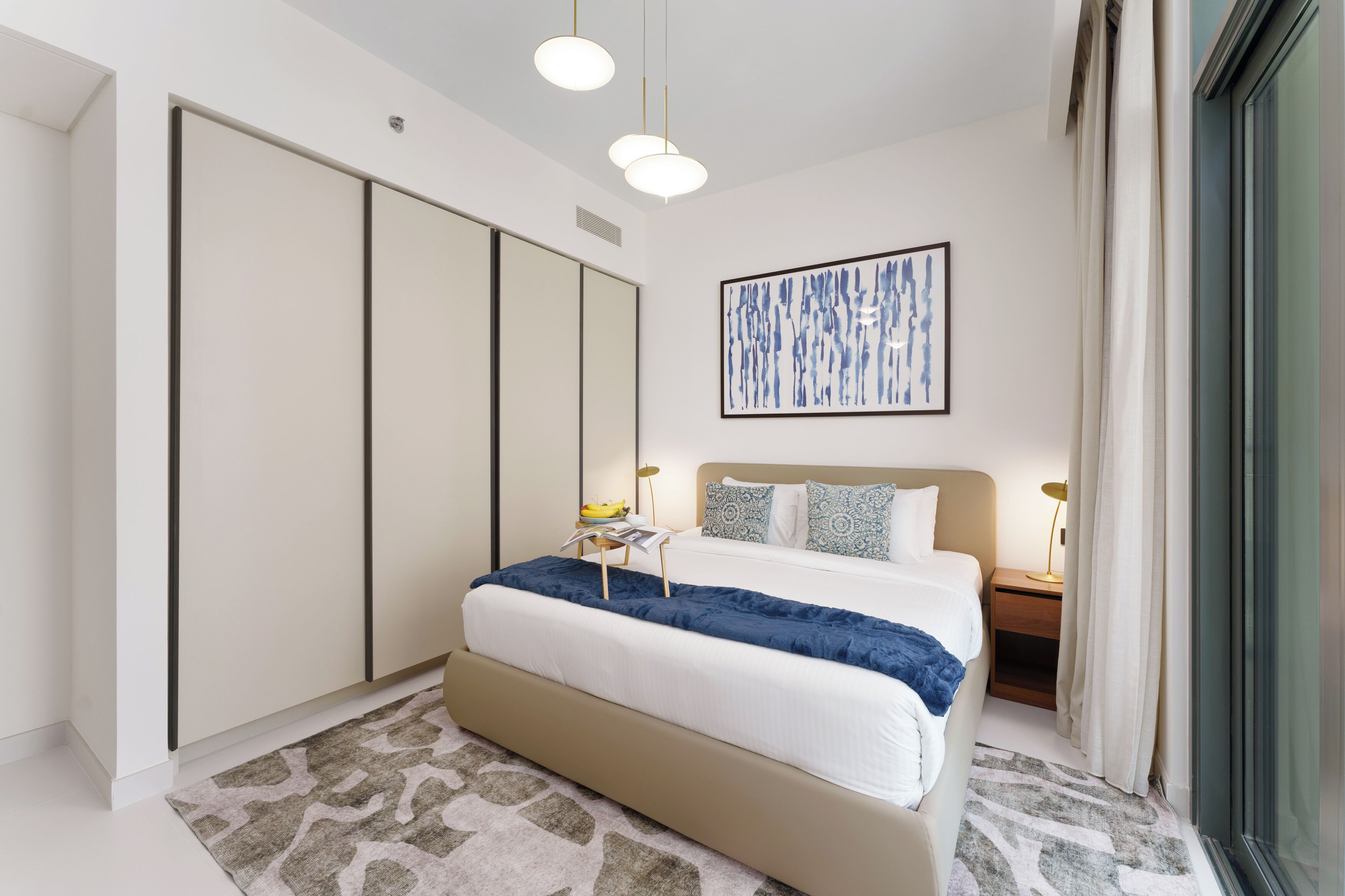 A modern bedroom with a large bed, a wardrobe, a bedside table with a lamp, and a large abstract painting on the wall.