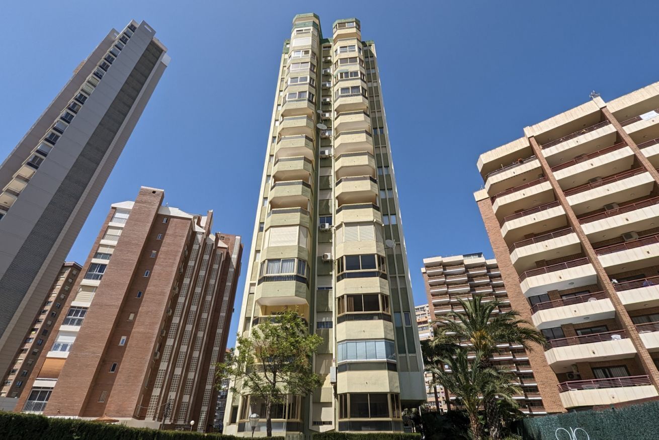 Un immeuble résidentiel de grande hauteur, doté de nombreux balcons et entouré d’autres bâtiments imposants.