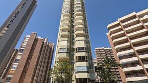 Un immeuble résidentiel de grande hauteur, doté de nombreux balcons et entouré d’autres bâtiments imposants.
