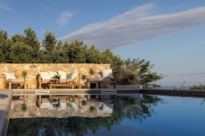 Un espace piscine agrémenté de murs en pierre, de chaises longues et offrant une vue sur les arbres.