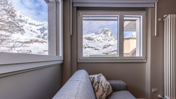 A cozy room with a gray sofa, a window with a snowy mountain view, and a radiator on the wall.
