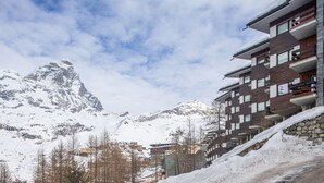 A modern hotel with multiple floors, a stone facade, and a view of snow-covered mountains.