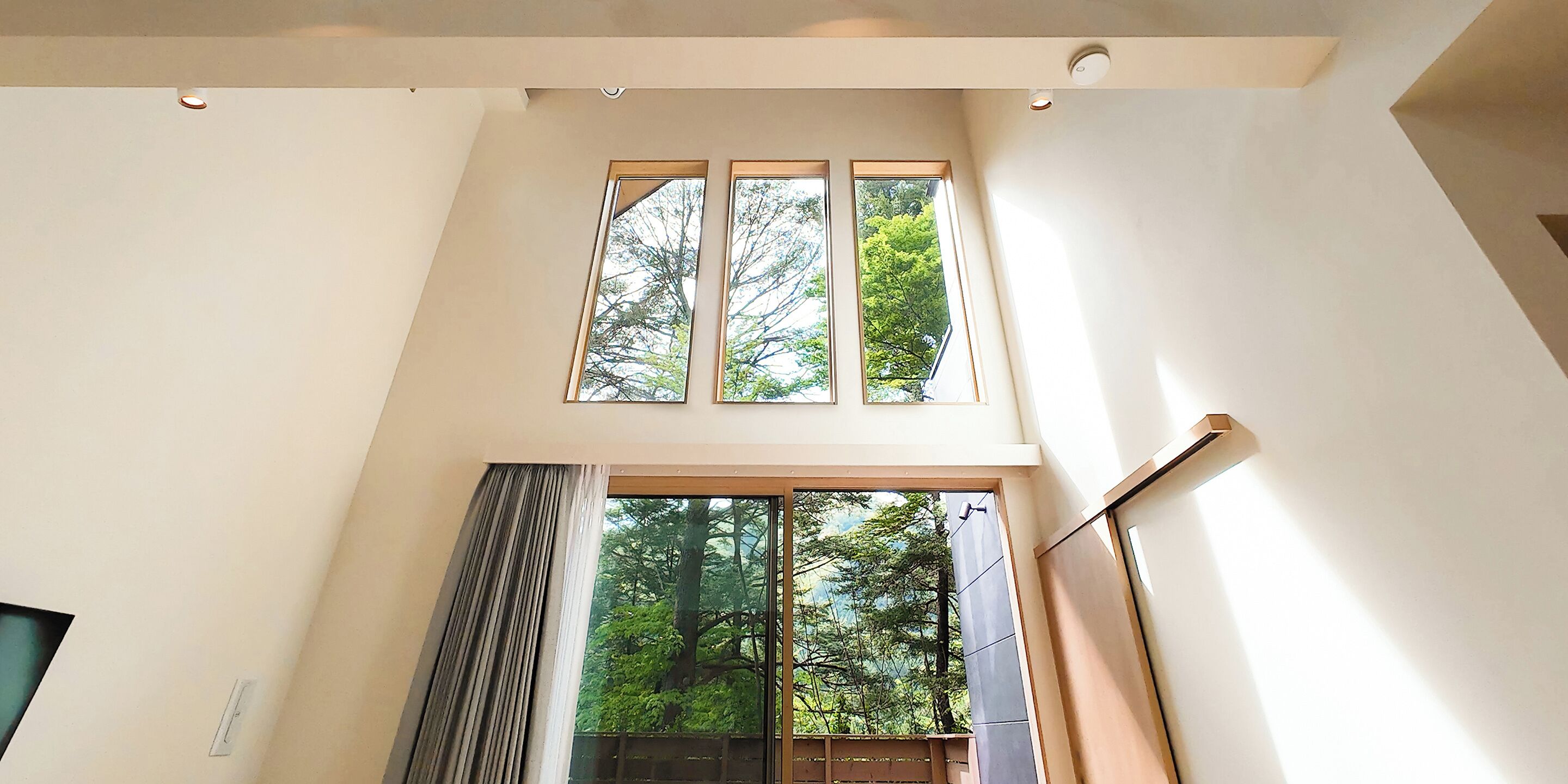 A high-ceiling room with a large window and a door leading outside.