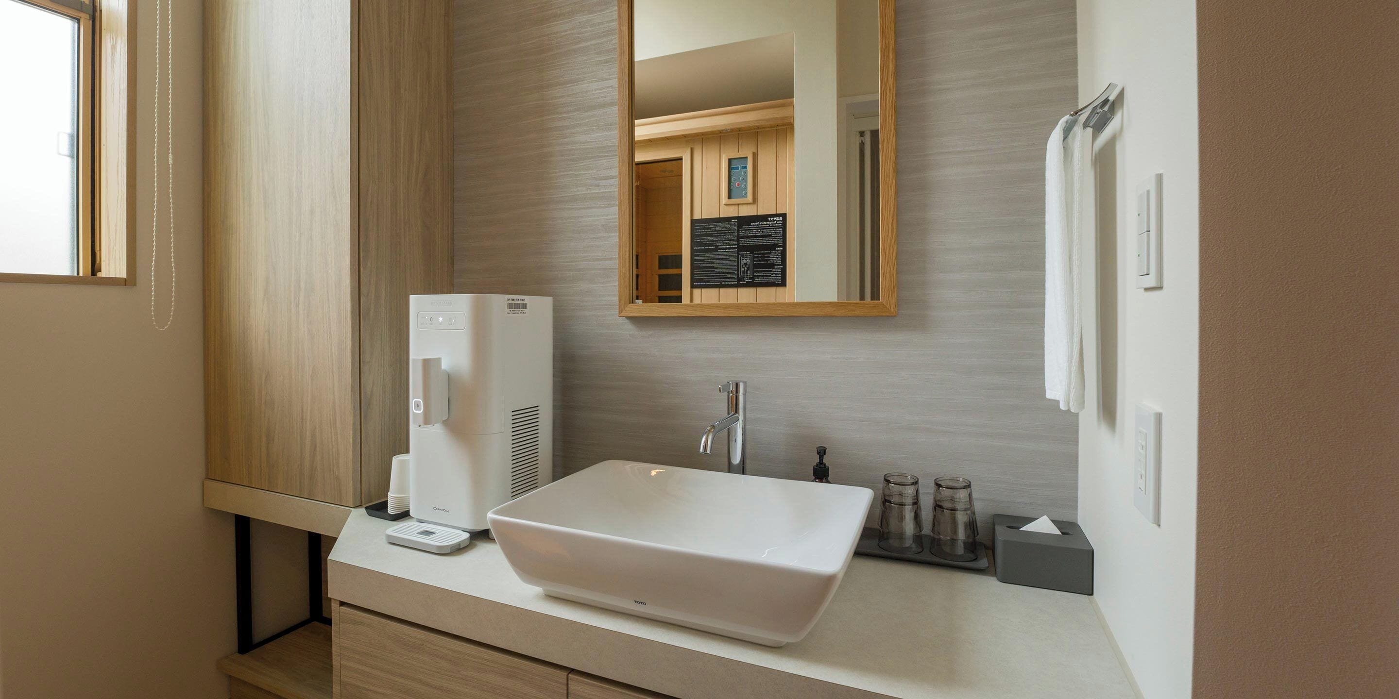 A modern bathroom with a large white sink, a mirror, a coffee machine, and a towel rack.