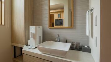 A modern bathroom with a large white sink, a mirror, a coffee machine, and a towel rack.