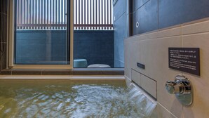 A modern bathroom with a large bathtub, a window with blinds, and a wall-mounted push button. - Rakuten STAY VILLA Kinugawa Riverside (Nikko)