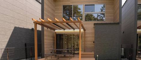 Un patio exterior moderno con una pérgola, una mesa de comedor y sillas.