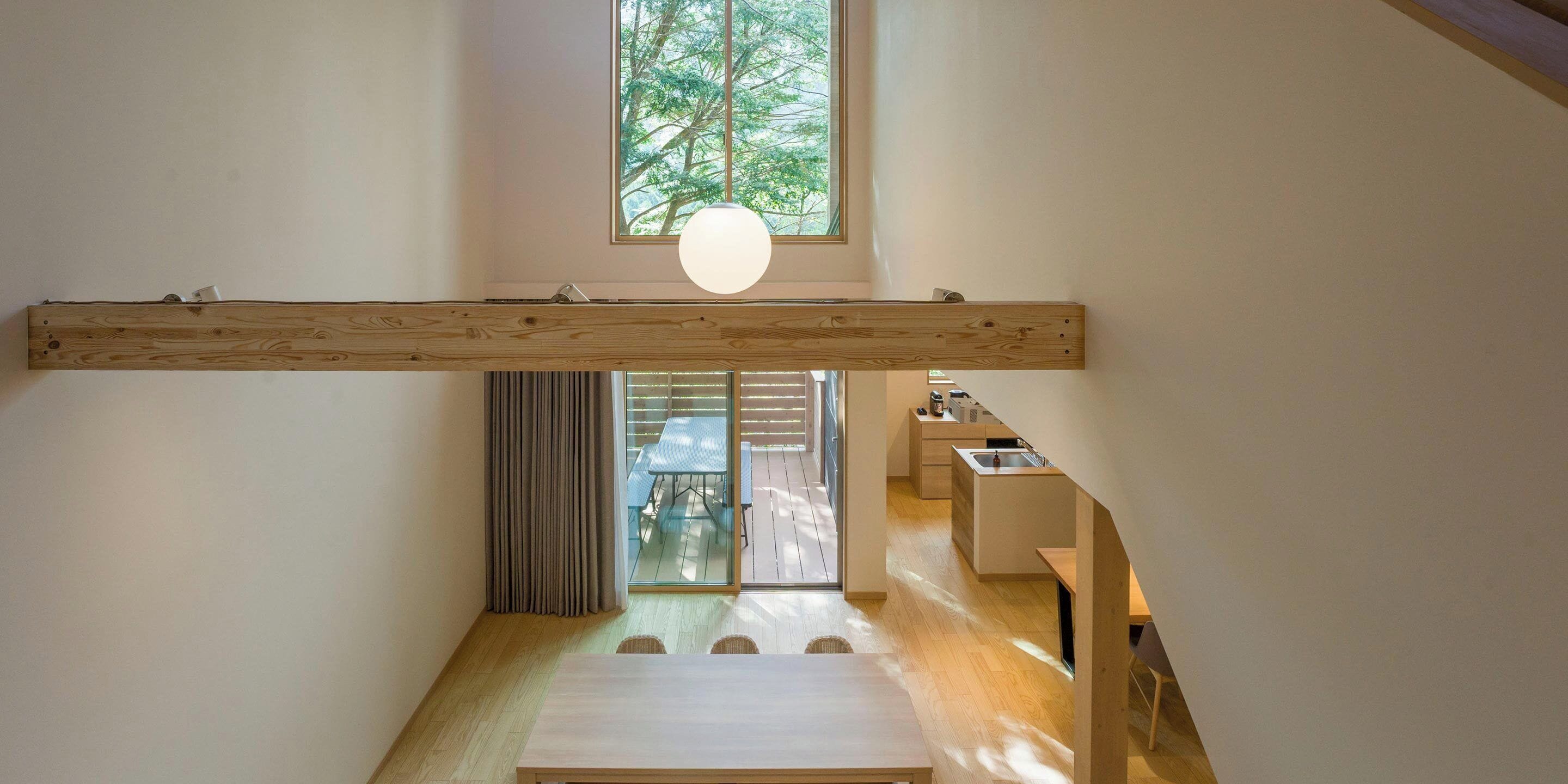 A modern interior with a high ceiling, wooden beams, a dining area with a table and chairs, and a view of a balcony with a table and chairs.