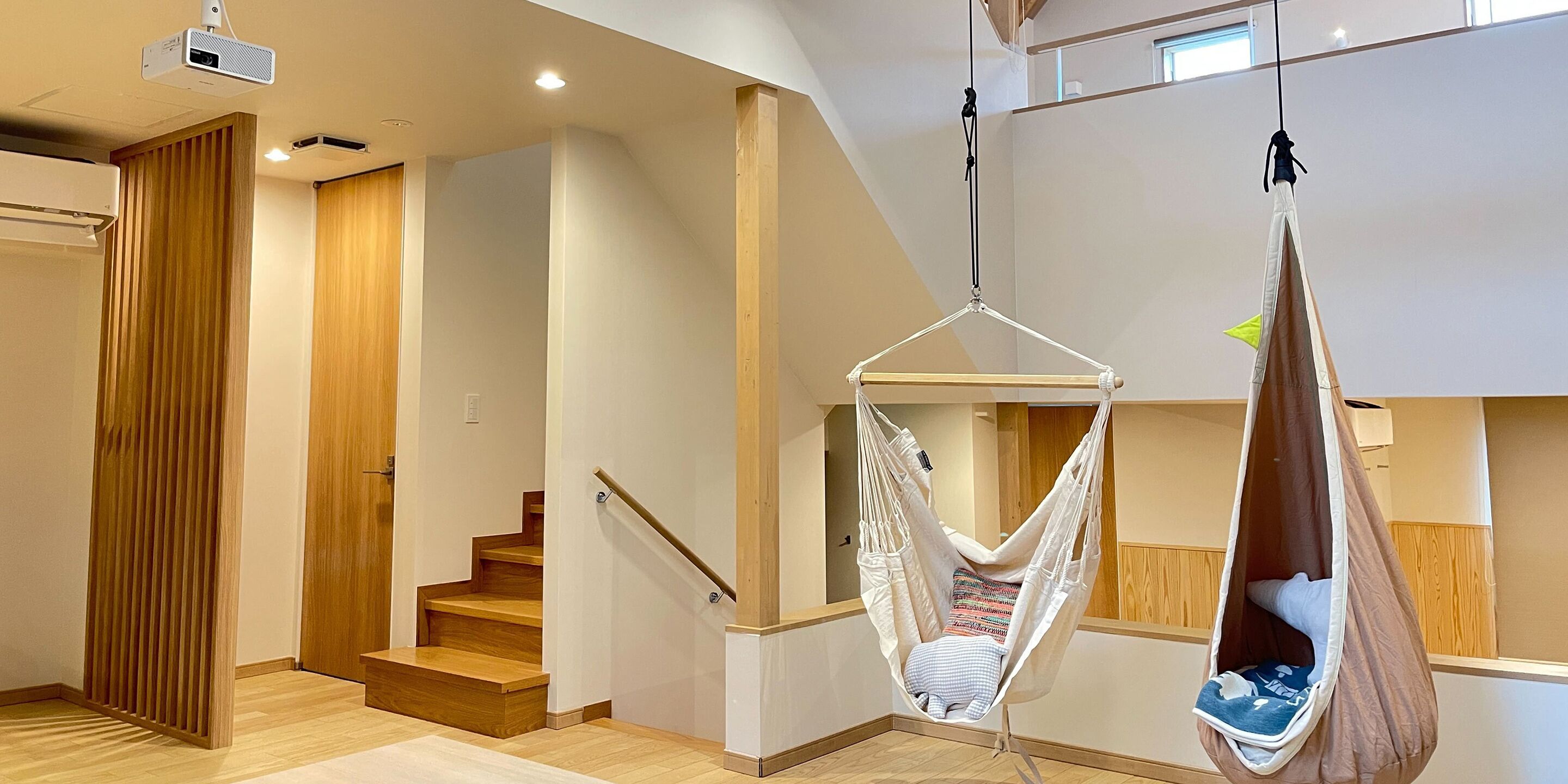 A modern interior with a wooden staircase, a white hanging chair, and a projector on the ceiling.