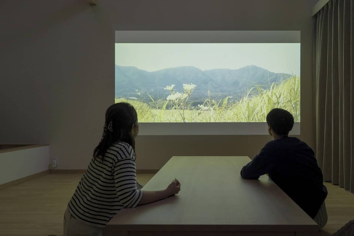 Two people sitting at a table in a room with a large window displaying a mountainous landscape.
