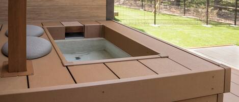 A hot tub with a wooden deck and a view of a fenced yard.