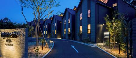 A row of modern, multi-story hotel buildings with a well-lit entrance and a clear road leading to the parking area.