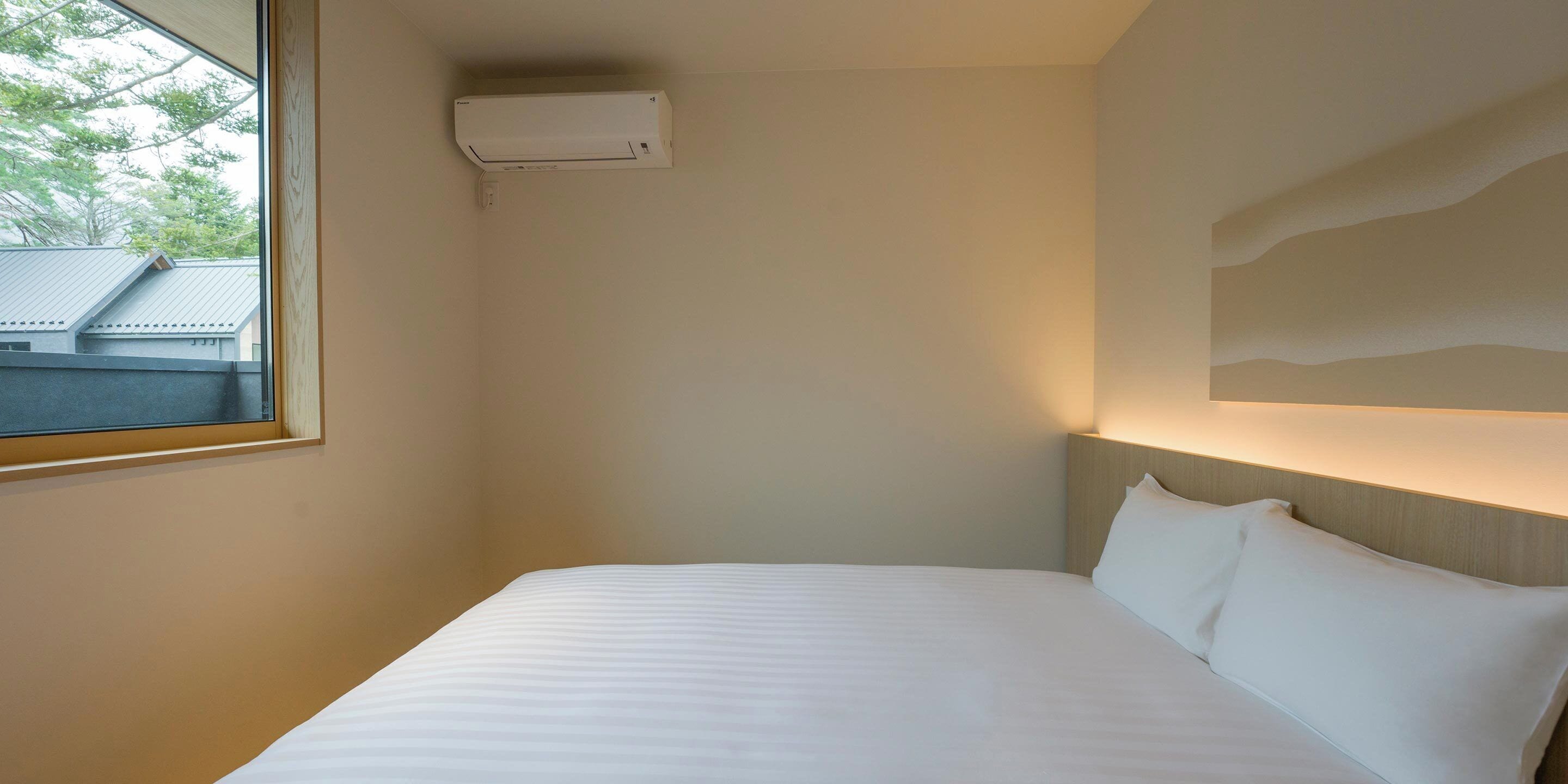 A hotel room with a bed, a window, and a wall-mounted air conditioner.