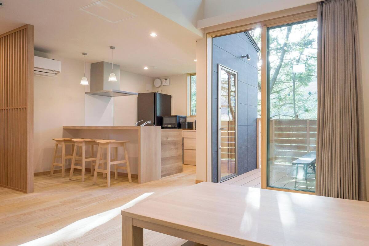 A modern kitchen with a bar area, wooden stools, and a large sliding glass door leading to a balcony.