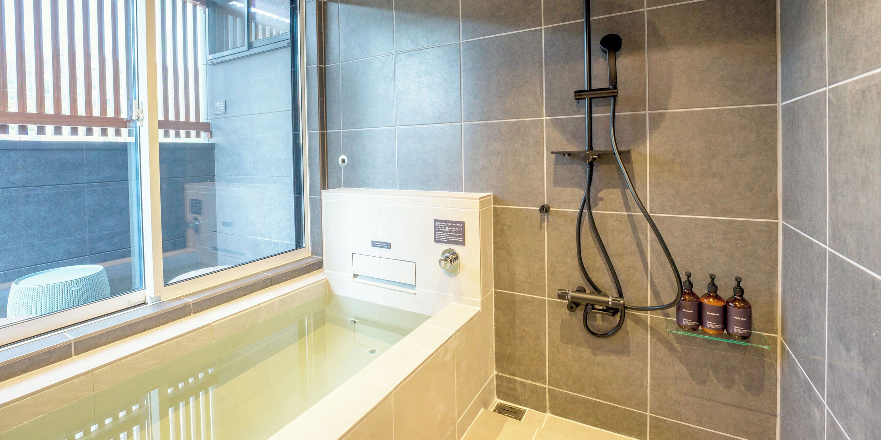 A modern bathroom with a glass-enclosed bathtub, a shower with a handheld showerhead, and a shelf with toiletries.