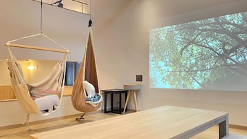 Una habitación con una hamaca colgante, una mesa y una pantalla que proyecta un árbol.
