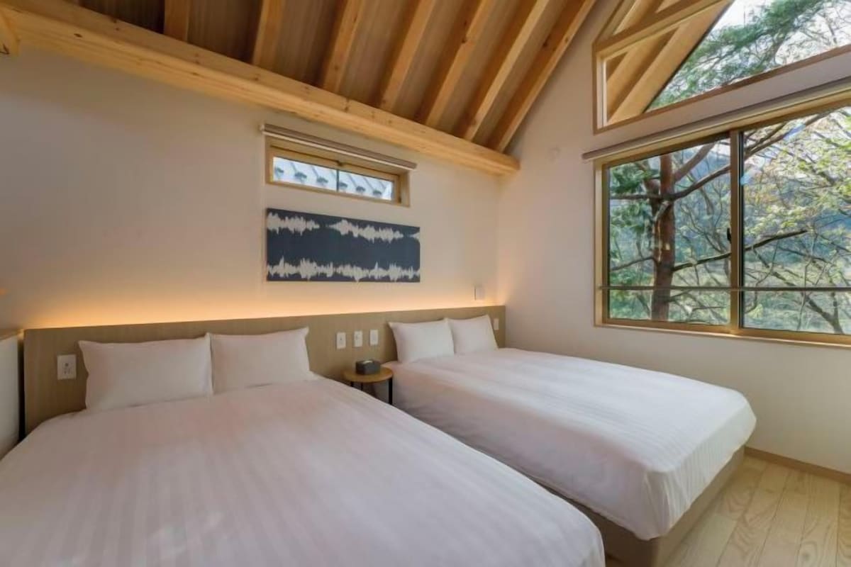 Ein Schlafzimmer mit zwei Betten, einem Fenster mit Blick auf Bäume und einem Gemälde an der Wand.