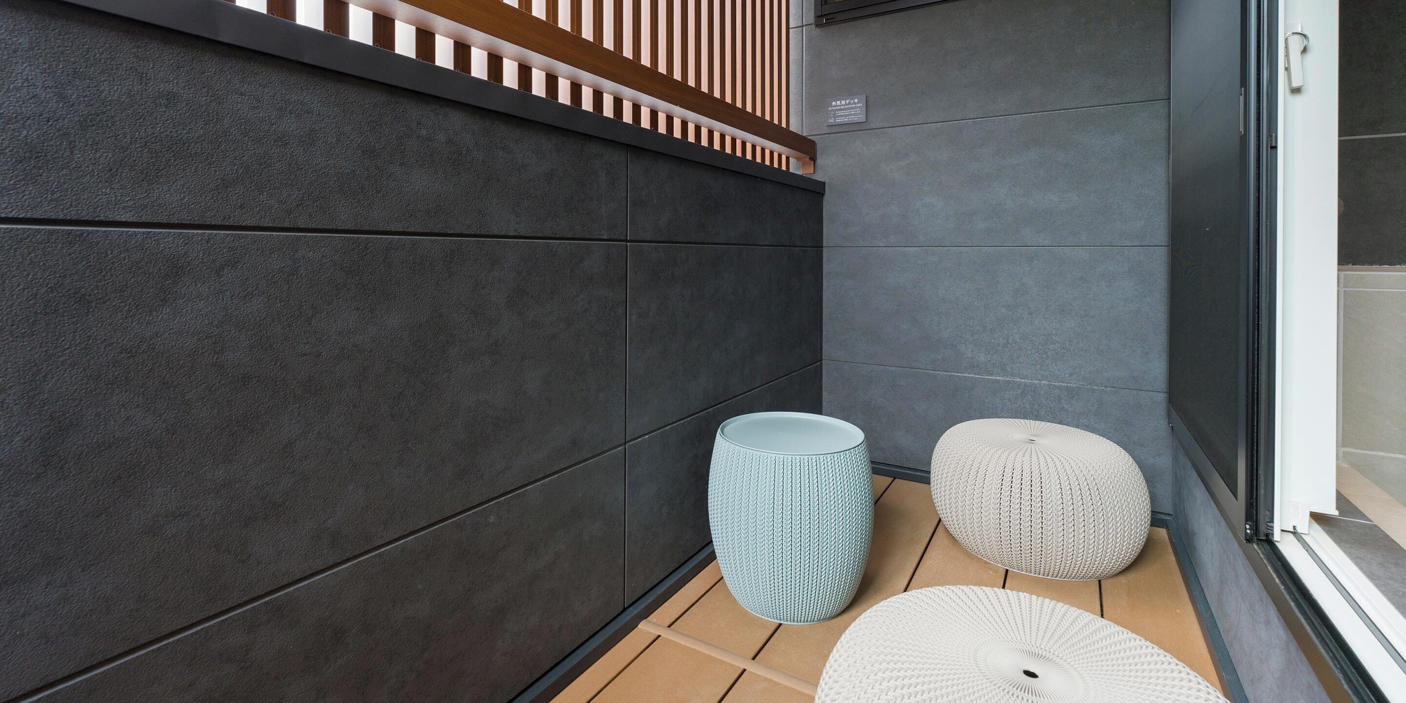 A modern bathroom with dark tiled walls, a wooden slatted partition, and two textured stools.