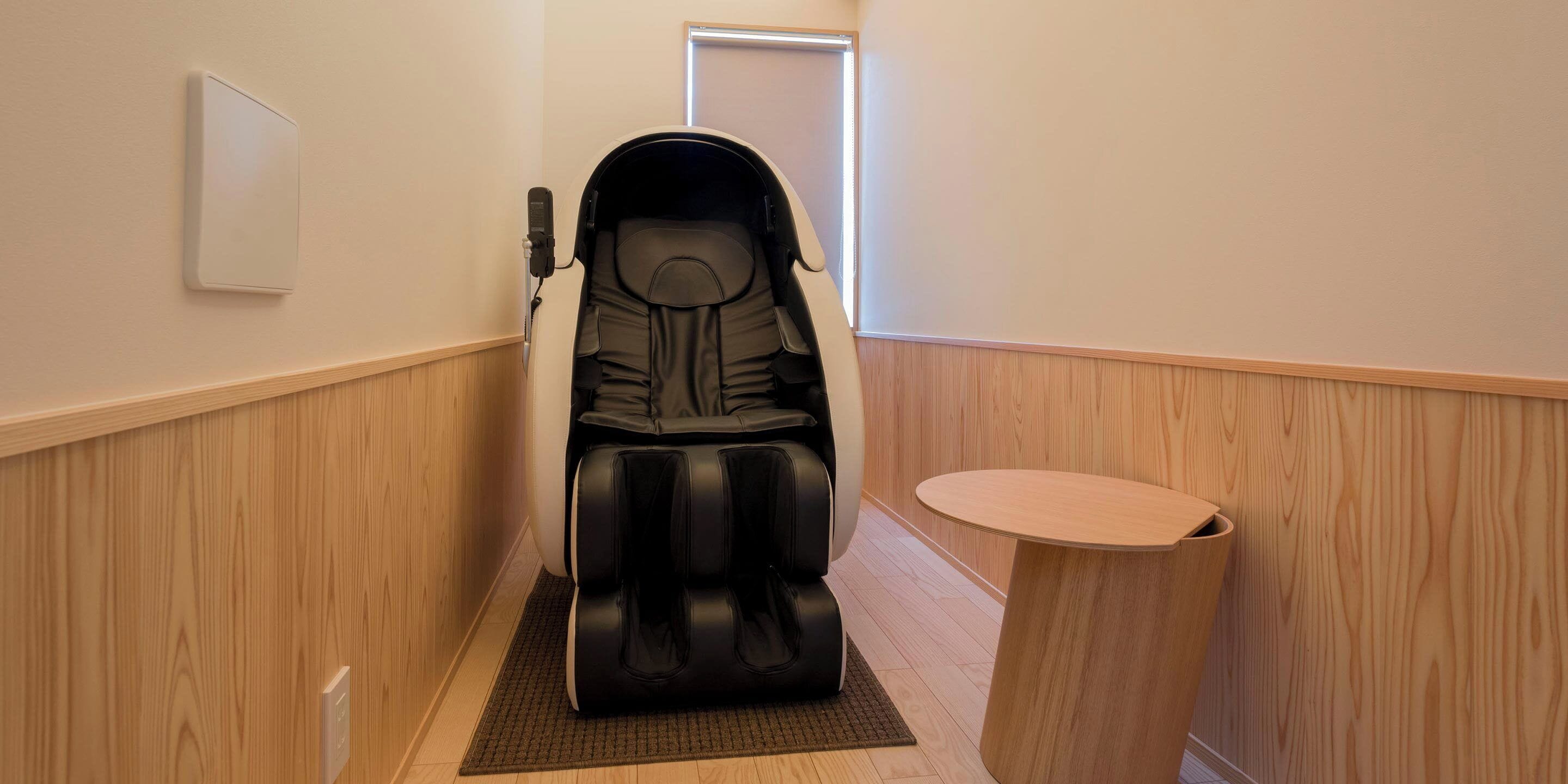 A massage chair in a hallway with wooden paneling, a small round table, and a door in the background.