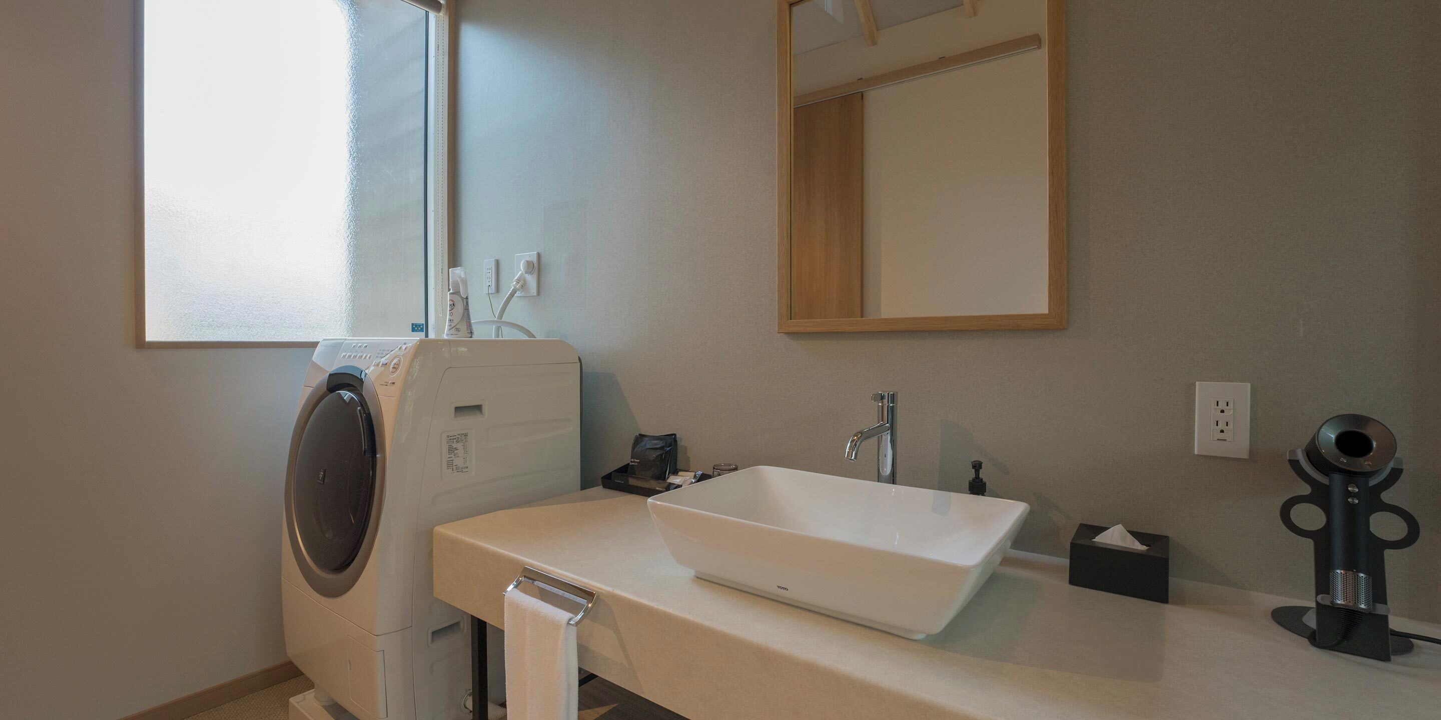 A modern bathroom with a built-in washing machine, a sink with a mirror above, and a towel rack.