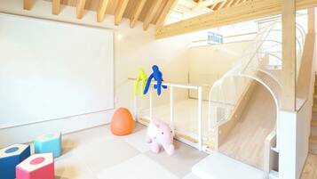 Zona de juegos infantiles con un tobogán, colchonetas blandas y juguetes coloridos.
