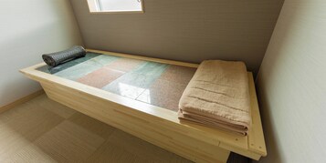 Una habitación pequeña y ordenada con un banco de madera, una toalla doblada y un felpudo en el suelo.