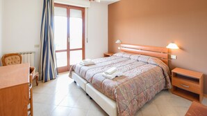A bedroom with a bed, a chair, a desk, and a window with curtains.