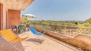 A balcony with two lounge chairs, a table, and an umbrella.