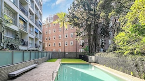 A swimming pool with a brick pathway, surrounded by a fence and trees. - Aquarius - Luxe Inner City Abode (Rushcutters Bay)