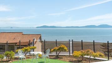 Propiedad costera con vista al mar, un jardín cercado con sillas y un edificio con tejado de tejas.