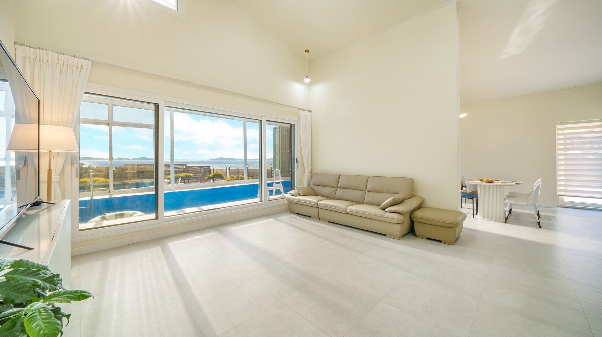 A spacious living area with a large window, a beige sofa, and a view of a pool.