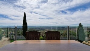 Un tavolo e due sedie in vimini di fronte a un panorama mozzafiato, incorniciato da una ringhiera in vetro.