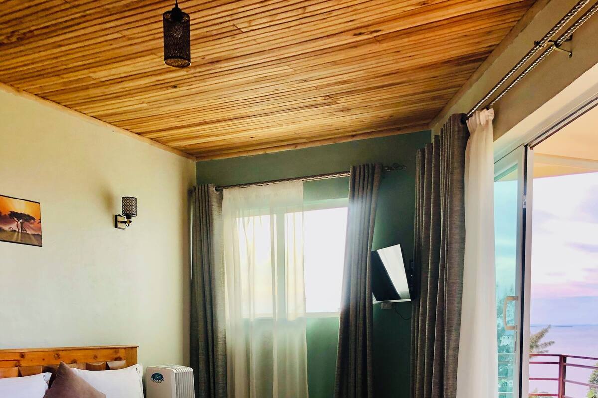 Un dormitorio con cama, mesita de noche, ventana con cortinas y vistas al exterior.