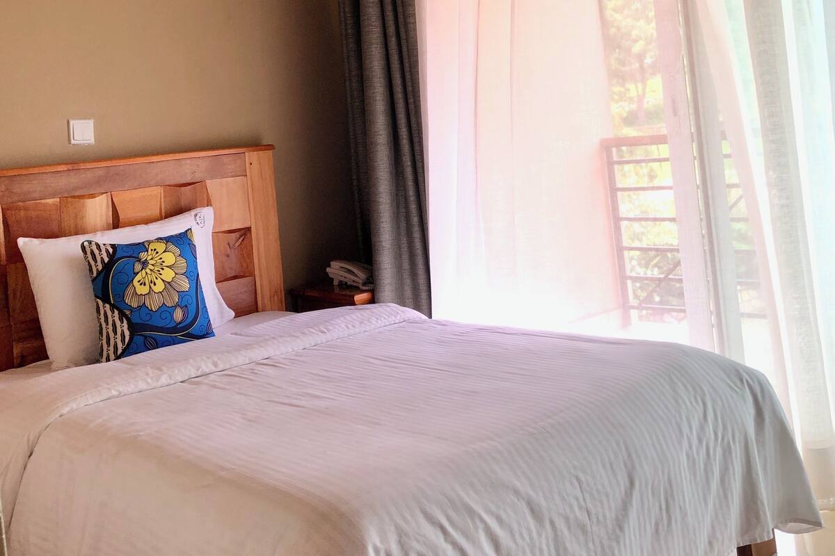Una cama bien hecha con sábanas blancas, un cabecero de madera y una almohada decorativa.