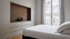 A bedroom with a bed, a built-in shelf, and a window with a view of buildings. - Sun-drenched Sophistication, by Veeve (Paris)