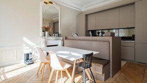 A modern dining area with a white table, two chairs, a bench, and a kitchen in the background. - Sun-drenched Sophistication, by Veeve (Paris)