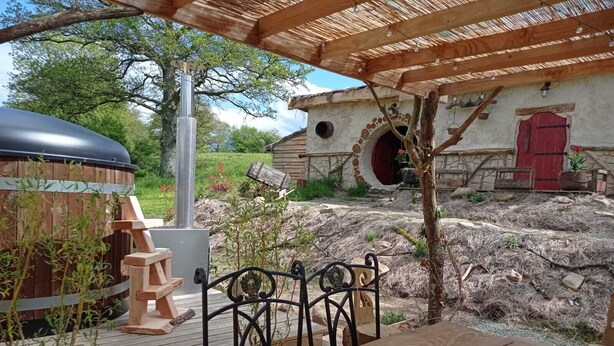 An outdoor patio with a wooden table and chairs, a hot tub, and a rustic stone wall in the background.