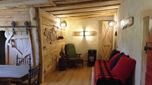 A rustic wooden room with a bed, a chair, a small table, and a wall-mounted heater.