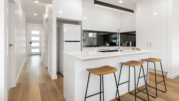 A modern kitchen with white cabinetry, a central island with stools, and a stainless steel range hood. - Lamington's Landing near Seacliff Beach (Seacliff Park)
