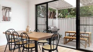 An indoor dining area with a wooden table and chairs, a grill, and a view through a glass door to an outdoor deck. - Lamington's Landing near Seacliff Beach (Seacliff Park)