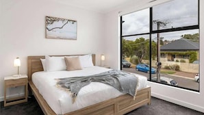 A bedroom with a large window, a bed, a bedside table, and a wall-mounted picture. - Lamington's Landing near Seacliff Beach (Seacliff Park)