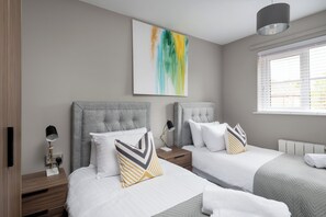 Two beds with grey headboards and white bedding, complemented by a contemporary abstract painting and a bedside table with a lamp.