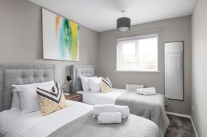 A hotel room with two beds, a large window with blinds, a modern pendant light, and a large abstract painting on the wall.