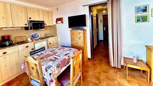 Ett kompakt kök med träskåp, en mikrovågsugn, en kaffebryggare och ett matbord med en mönstrad duk.