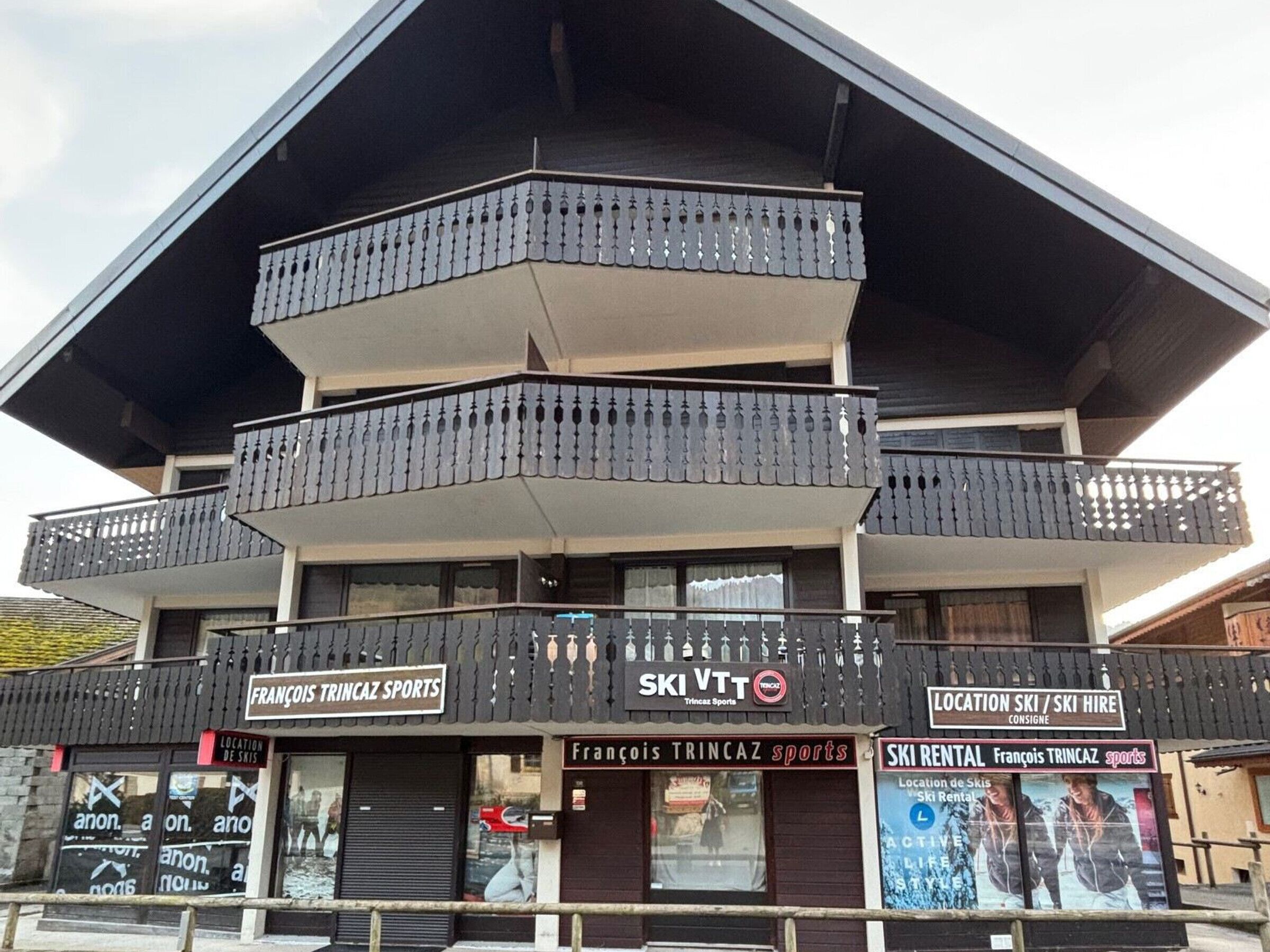 A multi-story building with balconies, signage for 'François Trincaz Sports' and 'Ski VTT', and a 'Location Ski / Ski Hire' sign.