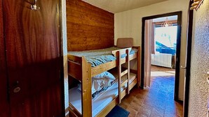 Ett litet rum med våningssängar, en trägarderob och utsikt genom en öppen dörr till ett utomhusområde.