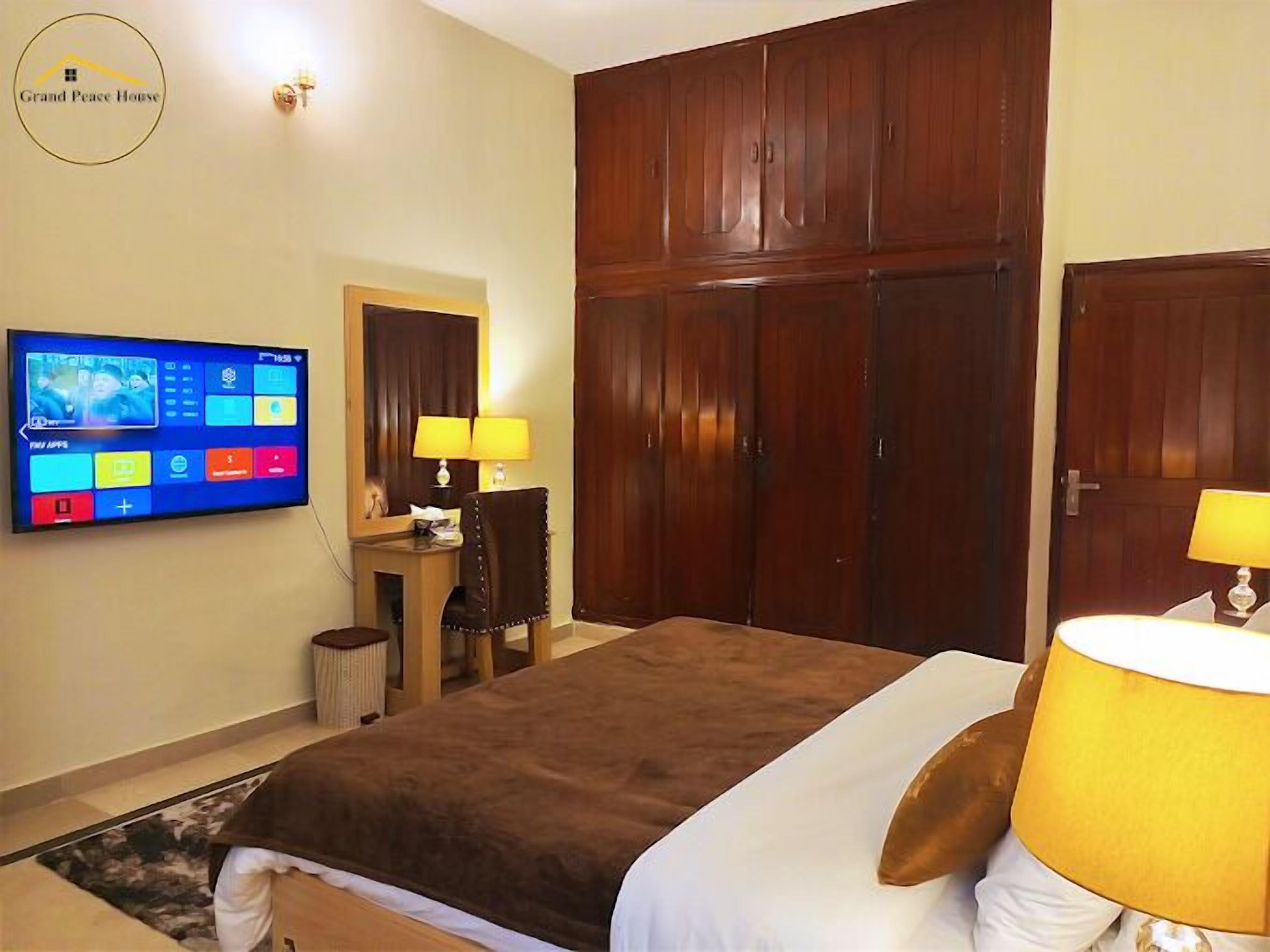 A hotel room with a large bed, a desk with a chair, a television mounted on the wall, and a wardrobe.