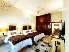 A hotel room with two beds, a large wardrobe, a ceiling fan, and a television.
