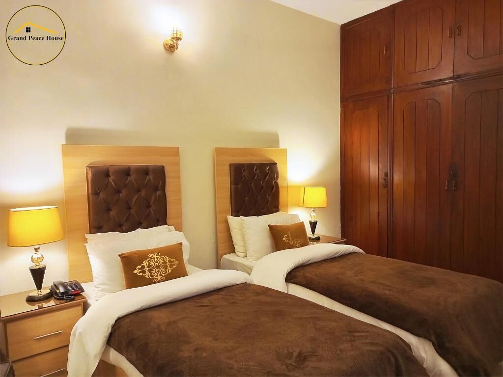 Habitación de hotel con dos camas, cabeceros de madera, lámparas de noche, un armario y un aplique de pared.